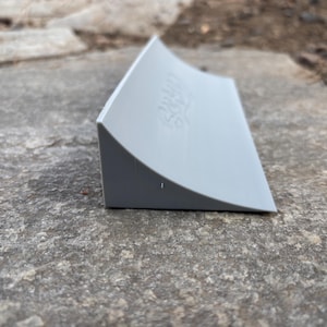 Puede incluir: Una rampa de pl&aacute;stico gris para fingerboard, con las palabras "24/7 Skate" impresas en el lateral.