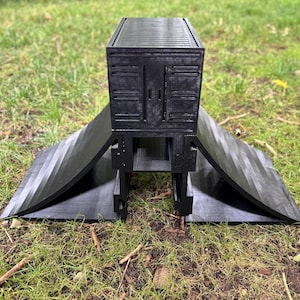 May include: A black, 3D-printed ramp structure with a rectangular top and angled side panels. The top section has a textured surface, and the side panels curve outward. The structure is designed to be placed on the ground.