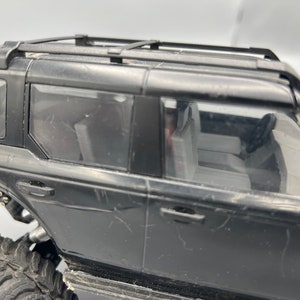 May include: Black toy SUV with a roof rack, visible windows, and detailed interior. The vehicle has large, rugged tires, suggesting an off-road design. The body shows some wear and tear.
