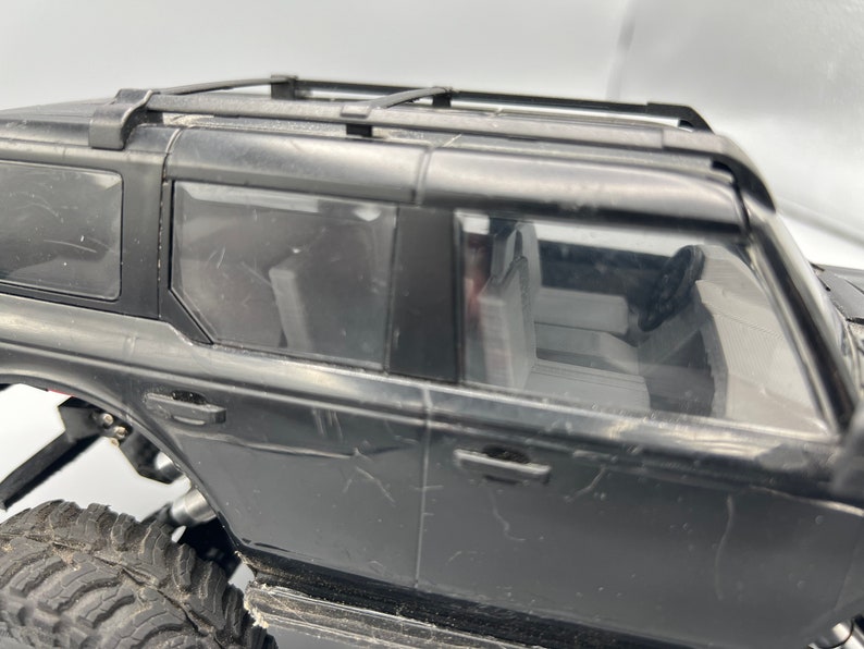 May include: Black toy SUV with a roof rack, visible windows, and detailed interior. The vehicle has large, rugged tires, suggesting an off-road design. The body shows some wear and tear.
