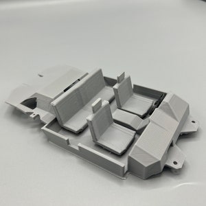 May include: A light gray 3D-printed model of a car interior, featuring seats and interior components. The model includes a front and back seat, and two individual front seats. The design is detailed, showing the layout of a vehicle's interior.