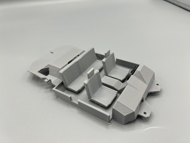 May include: A light gray 3D-printed model of a car interior, featuring seats and interior components. The model includes a front and back seat, and two individual front seats. The design is detailed, showing the layout of a vehicle's interior.