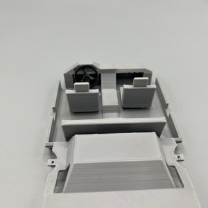 May include: A light gray 3D-printed model of a vehicle interior. The model includes a steering wheel, two seats, and a dashboard. The interior is a simplified representation of a car's cockpit.