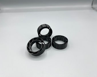Könnte beinhalten: Vier schwarze Kunststoffringe mit geometrischem Design. Die Ringe sind übereinander gestapelt.