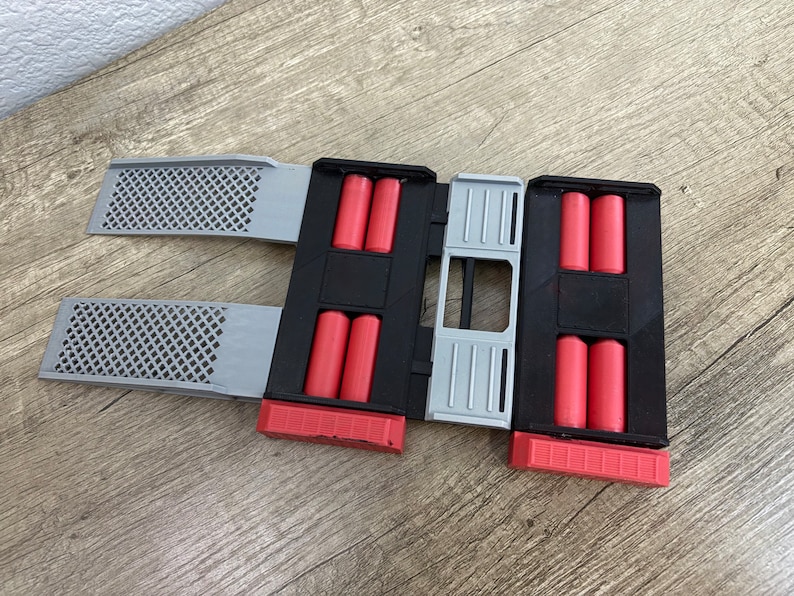 May include: A black and gray 3D-printed device with red cylindrical objects. The device has two gray, perforated panels extending from the sides. The device is designed to hold multiple red cylindrical objects.