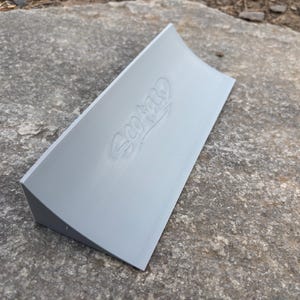 Puede incluir: Una rampa de skate de pl&aacute;stico gris con una superficie curva y la palabra "SCOOP" en relieve en la parte superior.