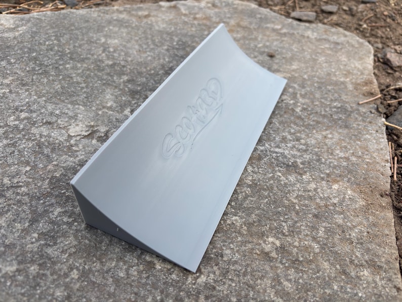 Puede incluir: Una rampa de skate de pl&aacute;stico gris con una superficie curva y la palabra "SCOOP" en relieve en la parte superior.