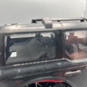 May include: A black toy SUV with a roof rack and tinted windows. The vehicle's interior is visible through the windows. The tires are partially visible on the left side of the image.
