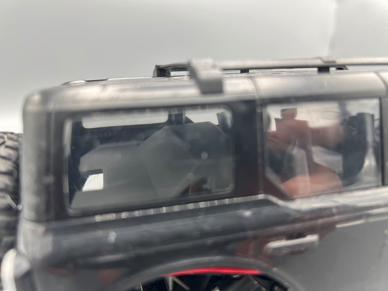 May include: A black toy SUV with a roof rack and tinted windows. The vehicle's interior is visible through the windows. The tires are partially visible on the left side of the image.