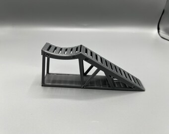 Könnte beinhalten: Eine graue Kunststoff-Auto-Rampe mit einer strukturierten Oberfläche und einer abgerundeten Oberseite. Die Rampe ist so konzipiert, dass sie die Räder eines Autos für Reparaturen oder Wartungsarbeiten anhebt.