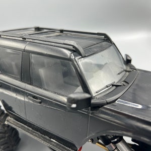 May include: Black toy SUV with a roof rack, side mirrors, and large off-road tires. The windshield wipers are visible. The vehicle is a detailed model, likely a replica of a popular SUV.