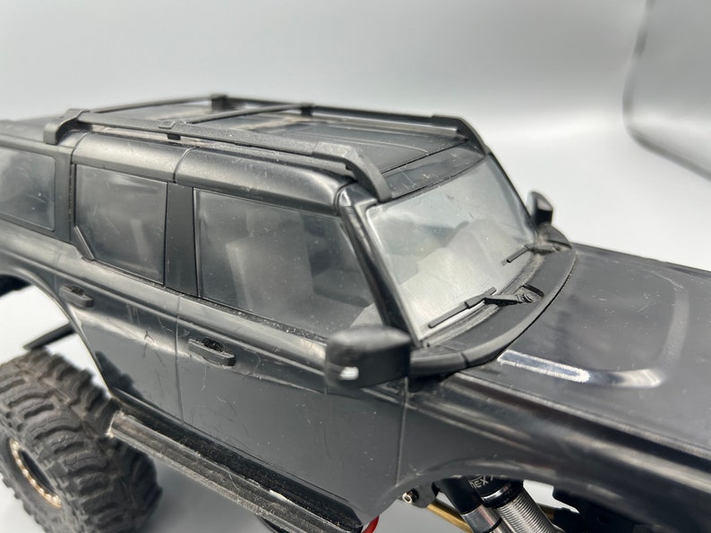 May include: Black toy SUV with a roof rack, side mirrors, and large off-road tires. The windshield wipers are visible. The vehicle is a detailed model, likely a replica of a popular SUV.