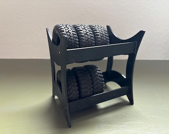 Könnte beinhalten: Ein schwarzer Reifenständer mit vier schwarzen Reifen, die auf zwei Regalen gestapelt sind. Der Ständer ist aus Kunststoff und hat ein schlichtes Design.