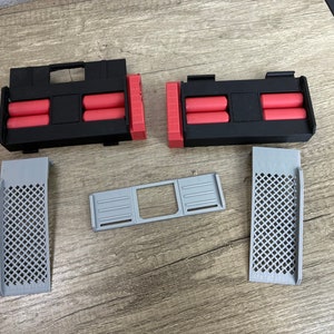 May include: An assortment of 3D-printed components in black, red, and gray. The set includes two black rectangular housings with red cylindrical inserts, two gray grilles with diamond patterns, and a gray rectangular frame.