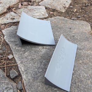 Könnte beinhalten: Zwei graue Plastikrampen zum Skateboarden. Die Rampen sind gebogen und haben eine leichte Lippe am Boden. Die größere Rampe hat den Schriftzug "SPRAY" aufgedruckt.