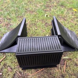 May include: Black, 3D-printed planter box with a slatted design, flanked by two matching curved supports. The planter box has a rectangular shape and is sitting on grass.