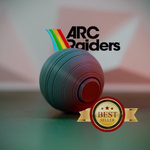 K&ouml;nnte beinhalten: Eine dunkelblaue und rote Rasen-Bowlingkugel mit dem Text "ARC Raiders" und einem Regenbogen-Design. Ein "Bestseller"-Siegel befindet sich im Vordergrund. Der Ball hat konzentrische Rillen und eine rote Mitte.