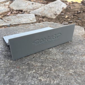 Puede incluir: Una cu&ntilde;a de pl&aacute;stico gris con el texto "Sea it Go" en relieve en la parte superior.