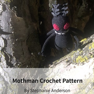 Może przedstawiać: Czarna, szydełkowa figurka Mothmana z czerwonymi oczami, osadzona na gałęzi drzewa. Figurka ma spiczasty łeb z koroną z piór. Tekst "Mothman Crochet Pattern" i "By Stephanie Anderson" znajduje się pod figurką.
