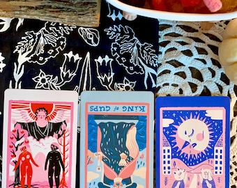 Puede incluir: Tres cartas de tarot sobre una superficie con estampado blanco y negro. Las cartas son "VI Los Enamorados", "REY de COPAS" y "XVIII La Luna".