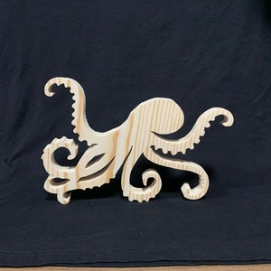 May include: A wooden cutout of an octopus with eight tentacles. The octopus is made of light brown wood and has a natural wood grain.