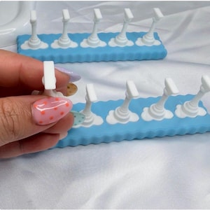 May include: Two rectangular light blue silicone stands featuring five white vertical pillars each. The pillars are attached to cloud-shaped bases on the blue rectangular platform. The stands have a scalloped edge design along the sides.