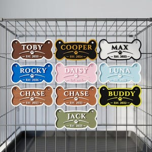May include: A collection of bone-shaped pet tags in various colors, each with a name and the year established. Names include Toby, Cooper, Max, Rocky, Daisy, Luna, Chase, Buddy, and Jack. The tags are displayed against a wire cage background.