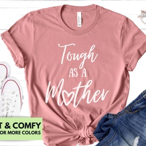 K&ouml;nnte beinhalten: Ein pinkfarbenes T-Shirt mit dem Text "Tough as a Mother" in wei&szlig;en Buchstaben, wobei ein Herz das "o" in "mother" ersetzt.