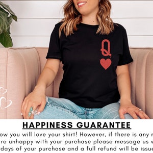 May include: A black t-shirt with a red queen of hearts graphic. The text "HAPPINESS GUARANTEE" is printed below the image. The text reads: "We know you will love your shirt! However, if there is any reason you are unhappy with your purchase please message us within 14 days of your purchase and a full refund will be issued."