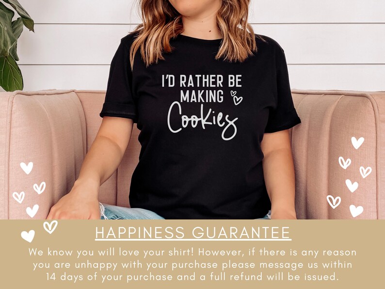 May include: A black t-shirt with the text "I'd rather be making cookies" in white lettering. The shirt is being worn by a person sitting on a pink couch. The text is surrounded by small white hearts.