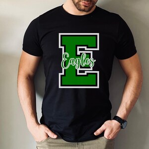 Puede incluir: Camiseta negra con una letra "E" verde y la palabra "Eagles" en letras blancas. La letra "E" est&aacute; delineada en blanco.