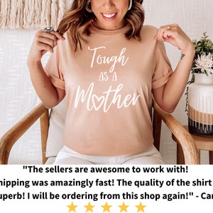 K&ouml;nnte beinhalten: Ein hellrosa T-Shirt mit dem Text "Tough as a Mother" in Wei&szlig;, wobei ein Herz das "o" in Mother ersetzt. Das Shirt wird von einer Person getragen.