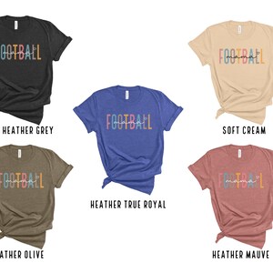 Op de afbeelding: Vijf verschillende gekleurde T-shirts met de tekst "FOOTBALL mama" in kleurrijke letters op de voorkant. De kleuren van de T-shirts zijn donker grijs gem&ecirc;leerd, zachte cr&egrave;me, heideblauw gem&ecirc;leerd, olijf gem&ecirc;leerd en heidepaars gem&ecirc;leerd.