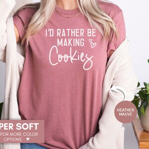 May include: A heather mauve t-shirt with the text "I'd rather be making cookies" in white lettering with two small hearts. The shirt is super soft and available in other colors.