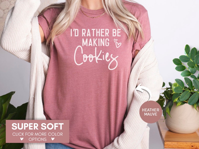 May include: A heather mauve t-shirt with the text "I'd rather be making cookies" in white lettering with two small hearts. The shirt is super soft and available in other colors.