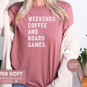May include: A heather mauve t-shirt with the text "Weekends Coffee and Board Games." printed in white. The shirt is super soft and available in other colors.