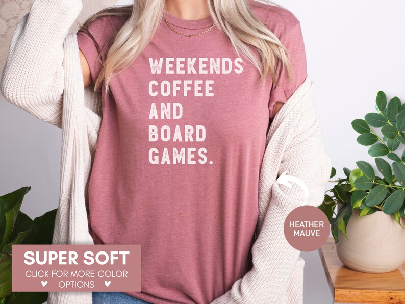 May include: A heather mauve t-shirt with the text "Weekends Coffee and Board Games." printed in white. The shirt is super soft and available in other colors.