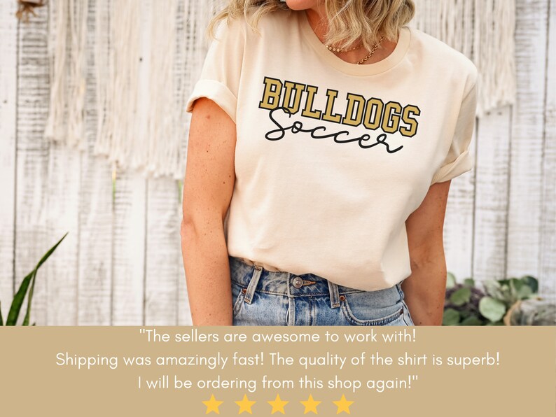 May include: A beige t-shirt with the text "BULLDOGS Soccer" in gold lettering. The shirt is being worn by a person. The text "The sellers are awesome to work with! Shipping was amazingly fast! The quality of the shirt is superb! I will be ordering from this shop again!" is displayed below the image.