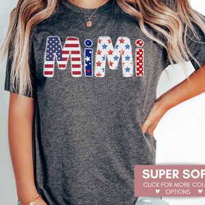 K&ouml;nnte beinhalten: Ein graues T-Shirt mit dem Wort "Mimi" in Rot, Wei&szlig; und Blau mit einem patriotischen amerikanischen Flaggenmuster. Der Text ist in einem abgenutzten, Vintage-Stil.