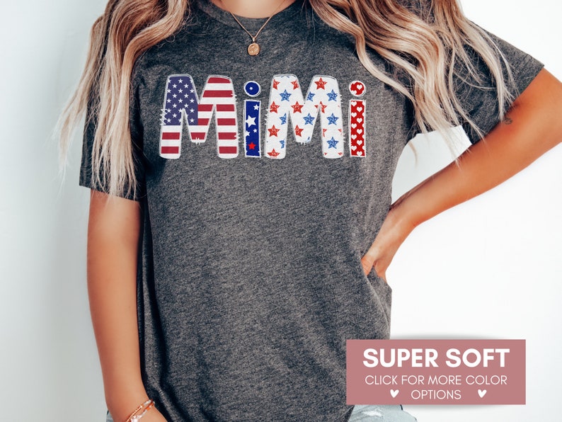 K&ouml;nnte beinhalten: Ein graues T-Shirt mit dem Wort "Mimi" in Rot, Wei&szlig; und Blau mit einem patriotischen amerikanischen Flaggenmuster. Der Text ist in einem abgenutzten, Vintage-Stil.