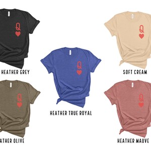 May include: Five different color t-shirts with a red queen of hearts graphic on the front. The colors are dark heather grey, soft cream, heather true royal, heather olive, and heather mauve.