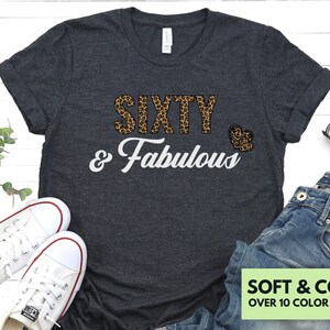 May include: A dark gray t-shirt with a leopard print design that says "Sixty & Fabulous" in white text. The shirt has a heart-shaped design with a leopard print pattern.