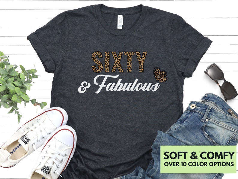 May include: A dark gray t-shirt with a leopard print design that says "Sixty & Fabulous" in white text. The shirt has a heart-shaped design with a leopard print pattern.
