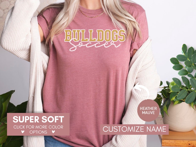 May include: A heather mauve t-shirt with the text "BULLDOGS Soccer" in gold lettering. The shirt is super soft and available in other colors. Customize the name on the shirt.