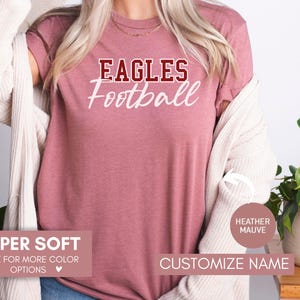 May include: A heather mauve t-shirt with the text "Eagles Football" in white and maroon lettering. The shirt is super soft and available in other colours.