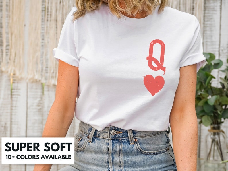 May include: White t-shirt with a red queen of hearts graphic. The graphic is a stylized queen of hearts card with a red heart and the letter Q.