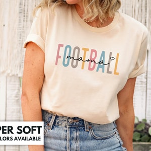 Op de afbeelding: Een cr&egrave;mekleurig T-shirt met de tekst "FOOTBALL mama" in regenboogkleuren. De tekst is in een gestileerd lettertype met een hartje na "mama".