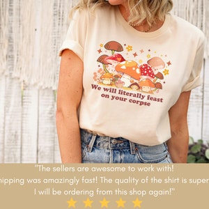Op de afbeelding: Een beige t-shirt met een afbeelding van paddenstoelen en de tekst "We will literally feast on your corpse".