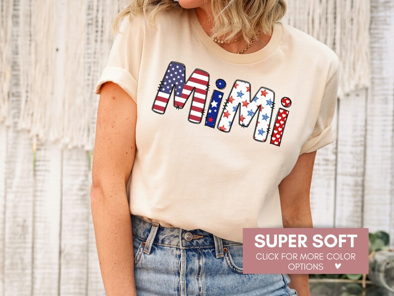K&ouml;nnte beinhalten: Ein beiges T-Shirt mit dem Wort "Mimi" in den patriotischen Farben Rot, Wei&szlig; und Blau. Die Buchstaben sind mit Sternen und Herzen verziert.