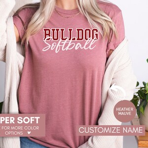 May include: A heather mauve t-shirt with the text "BULLDOG Softball" in white and maroon lettering. The shirt is super soft and available in other colors. Customize the name on the shirt.